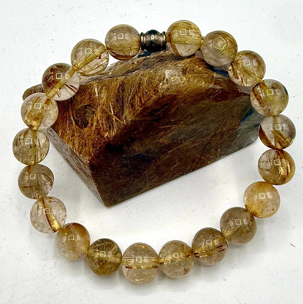 Golden rutilated quartz bracelet featuring polished beads, crafted by STICS and STONES, displayed on a neutral background.